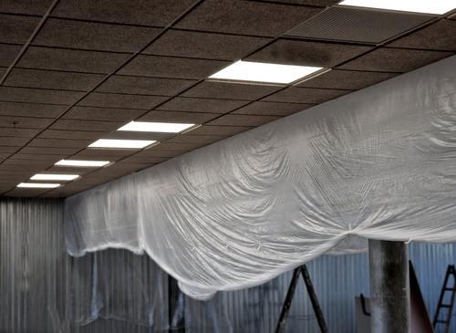 Acoustic ceiling renovation in progress with brown sound-absorbing tiles and plastic sheeting protecting the interior space during commercial ceiling work