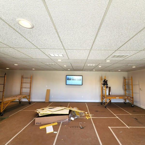 Renovation of acoustic ceiling tiles in a multipurpose room with scaffolding and lighting