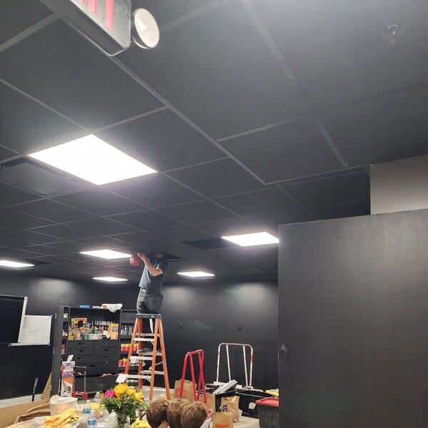 Technician installing black drop ceiling tiles in a modern dark-themed room