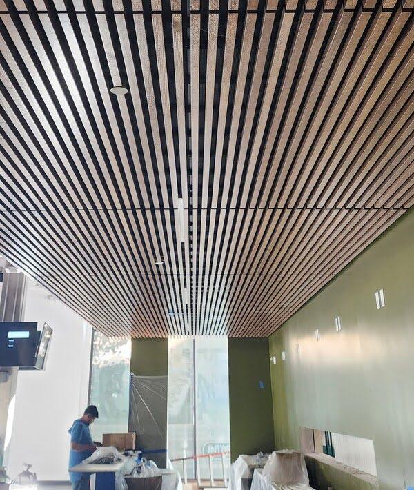 Installation of slatted wood ceiling panels in a modern commercial space, offering a stylish and acoustic-friendly ceiling solution