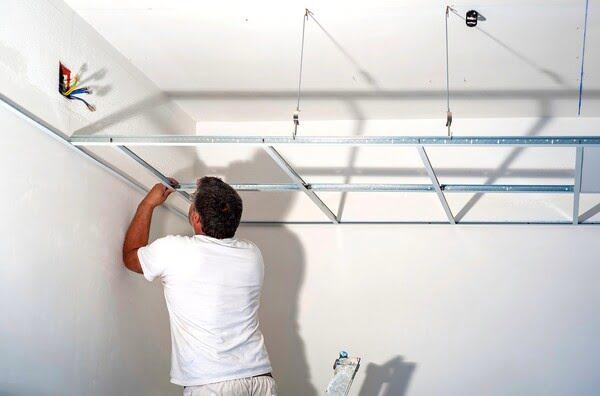 Contractor installing a T-Bar ceiling grid system for a suspended ceiling, securing metal framing to wall brackets during early installation phase