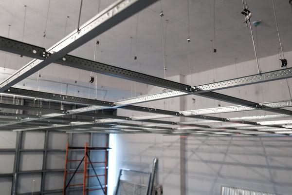 Suspended T-Bar ceiling grid installation with metal framing and wire hangers in a commercial construction setting, ready for ceiling tile placement
